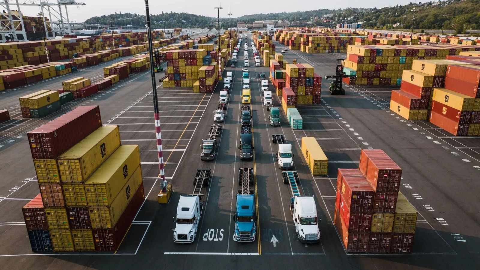 Stacked shipping containers with trucks queuing in a port yard